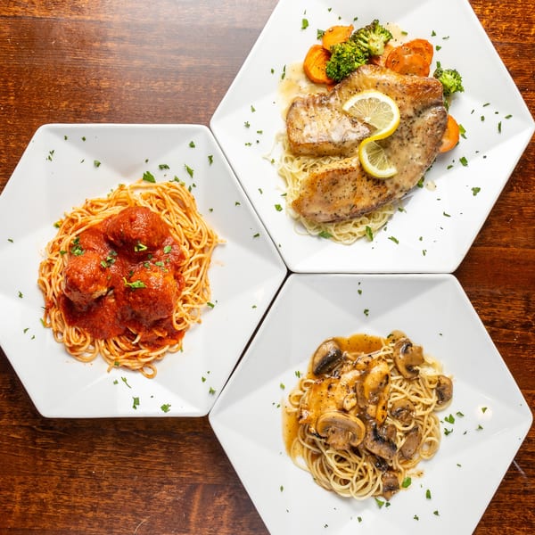 Three Italian dishes on white hexagonal plates: spaghetti with meatballs, lemon fish with vegetables, and chicken marsala.