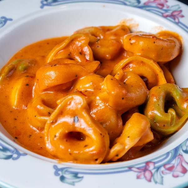 Close-up of cheese tortellini in a creamy orange sauce, served in a white bowl with a floral rim.
