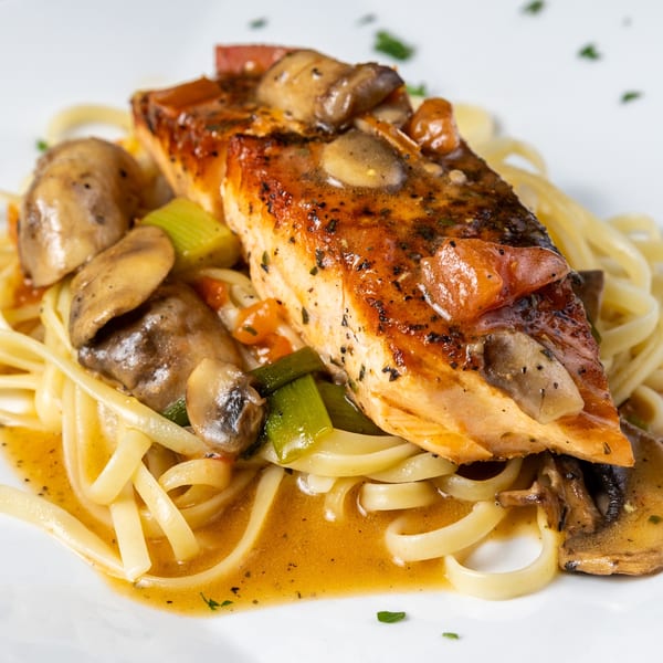 Grilled salmon with mushrooms and vegetables over linguine pasta in a savory sauce.